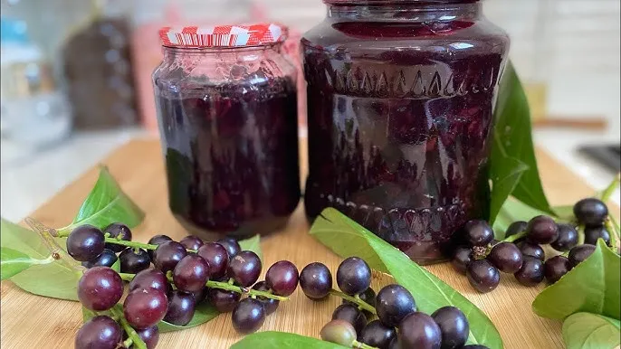 An image of two jars of dark red jam, with fresh cherry laurel fruit in front.